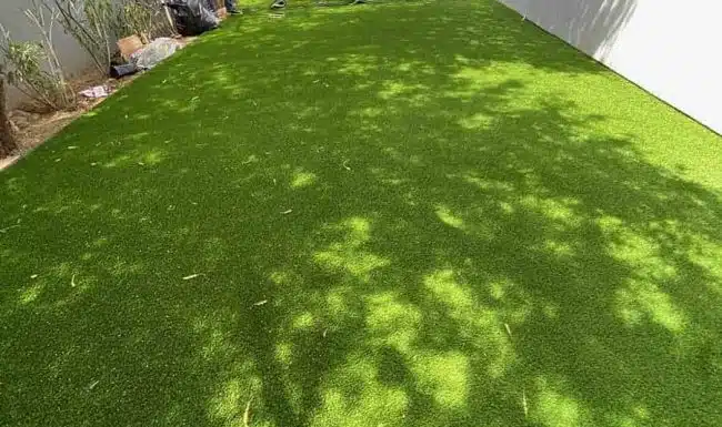 Close-up of newly installed artificial turf in a narrow backyard space with tree shadows.