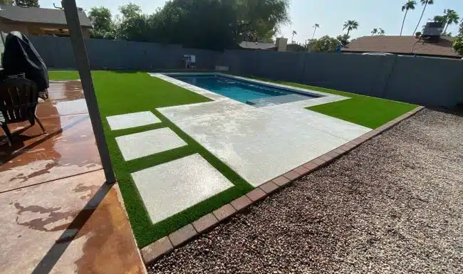 Artificial turf installation around a rectangular swimming pool with stepping stones and concrete patio in a sunny backyard.