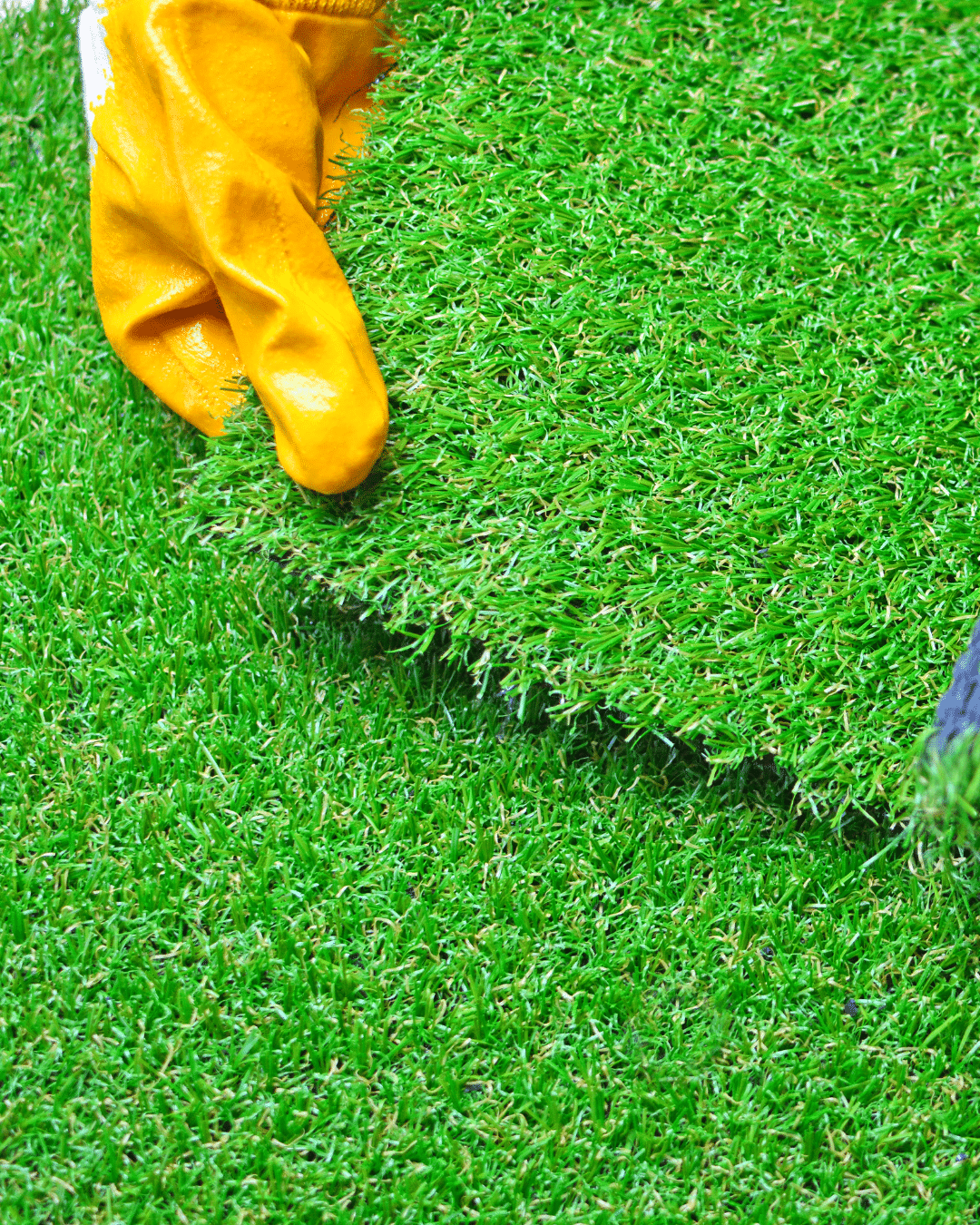 A hand in a yellow glove installing a roll of artificial turf.