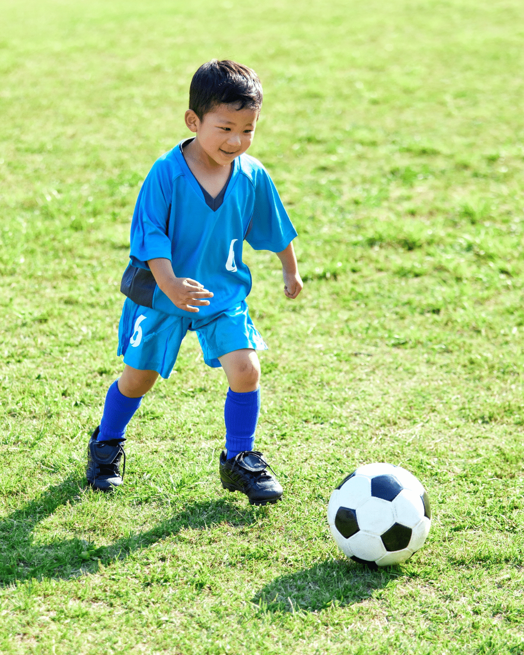 Young boy in blue soccer uniform dribbling a ball on a bright green turf field.